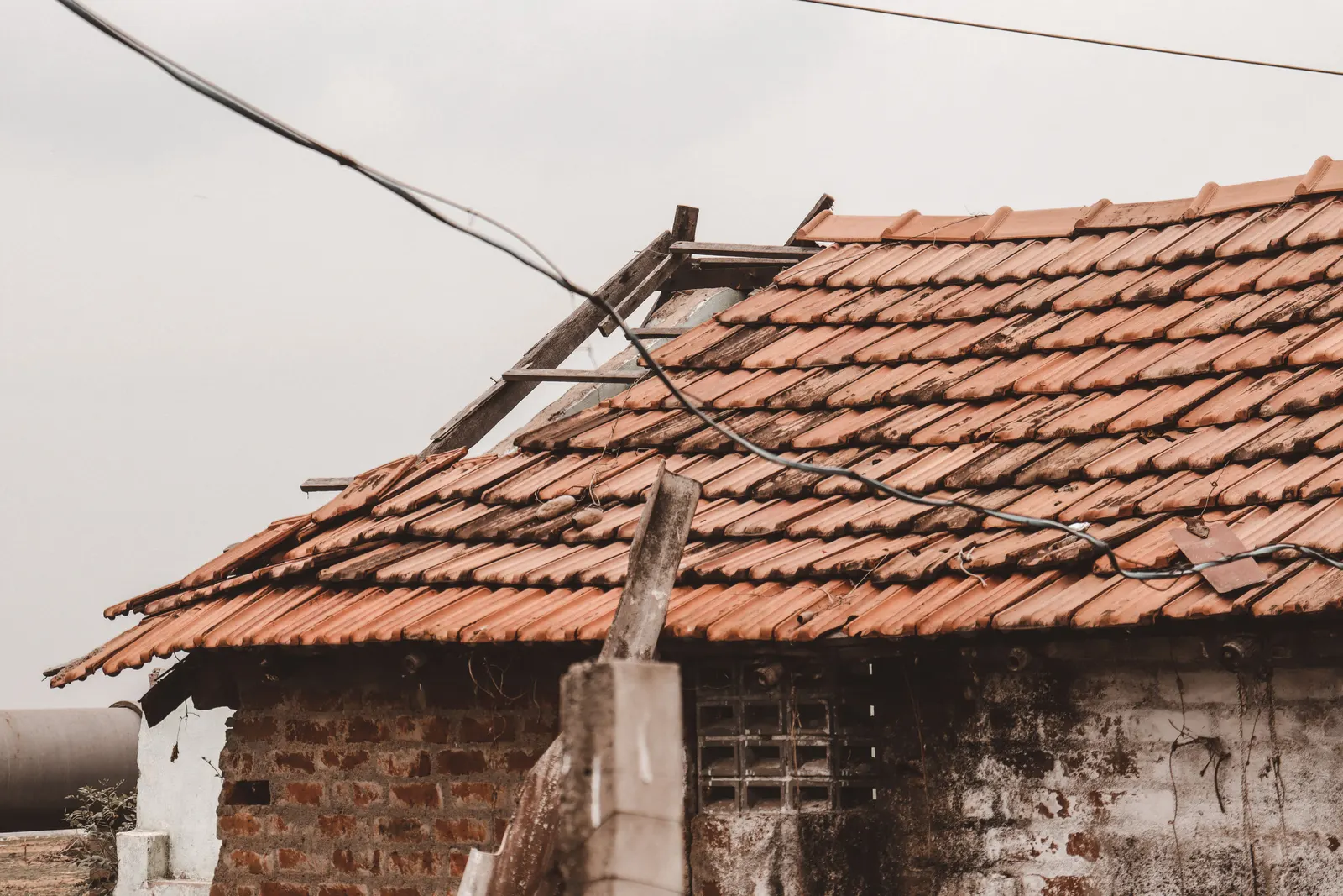 An aged tile roof with a section stripped back and tiles missing above a damaged wall.