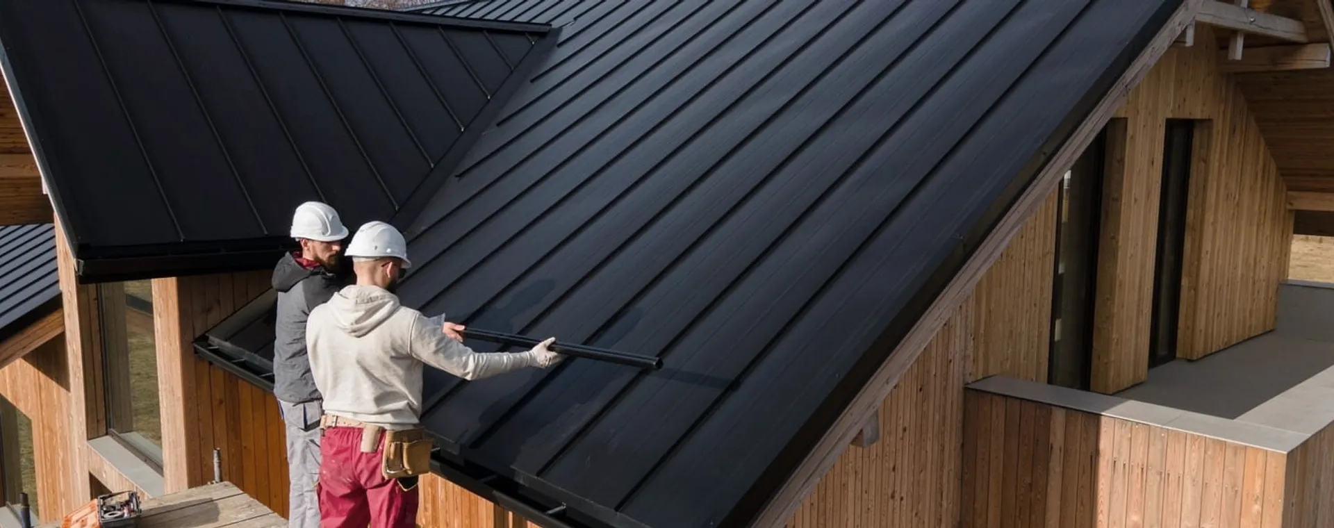 Two roofers in helmets on a black metal roof.