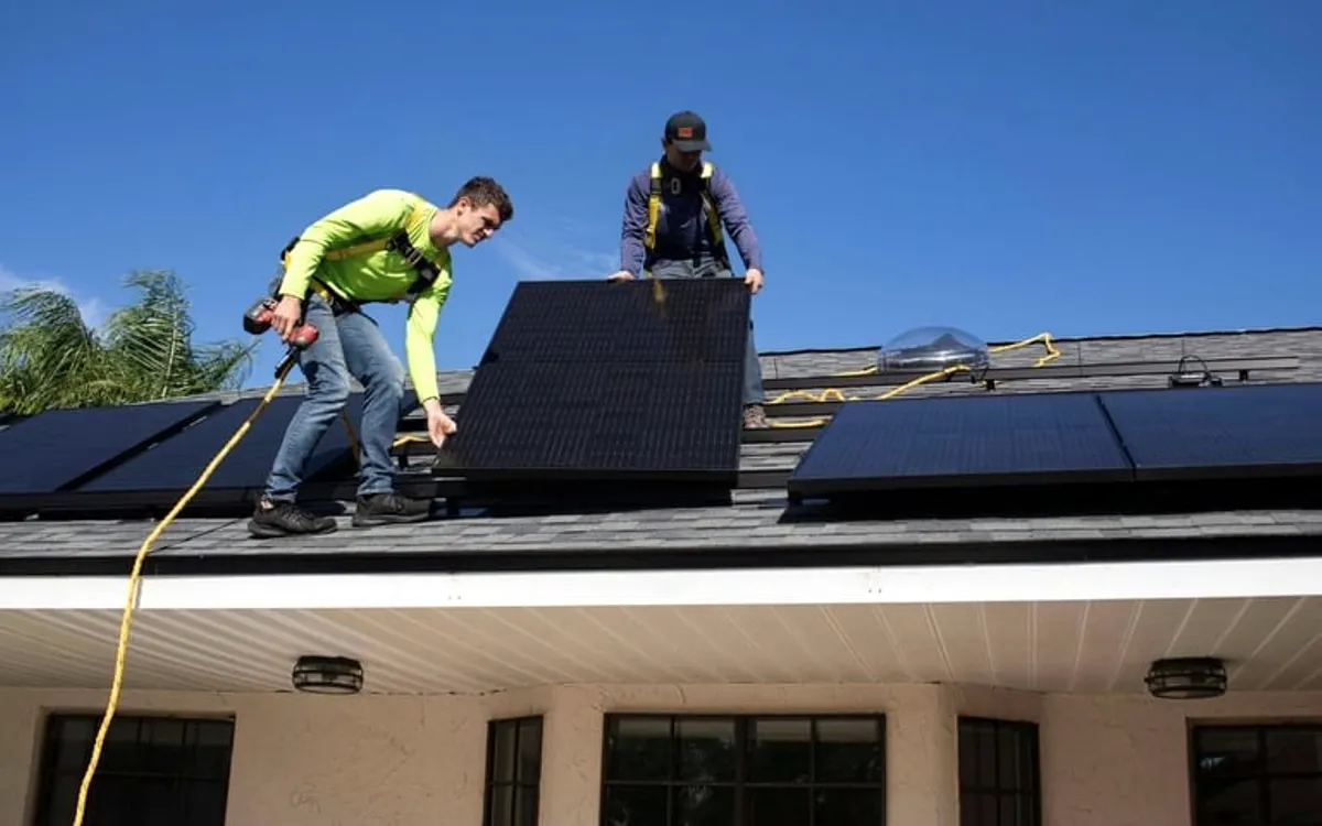 Two roofers fitting panels on a roof.