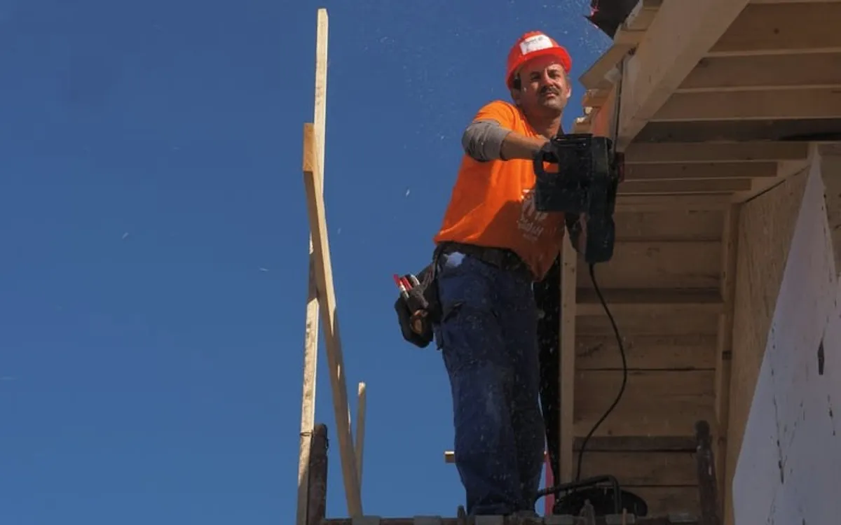 A roofer in an orange shirt framing a roof.