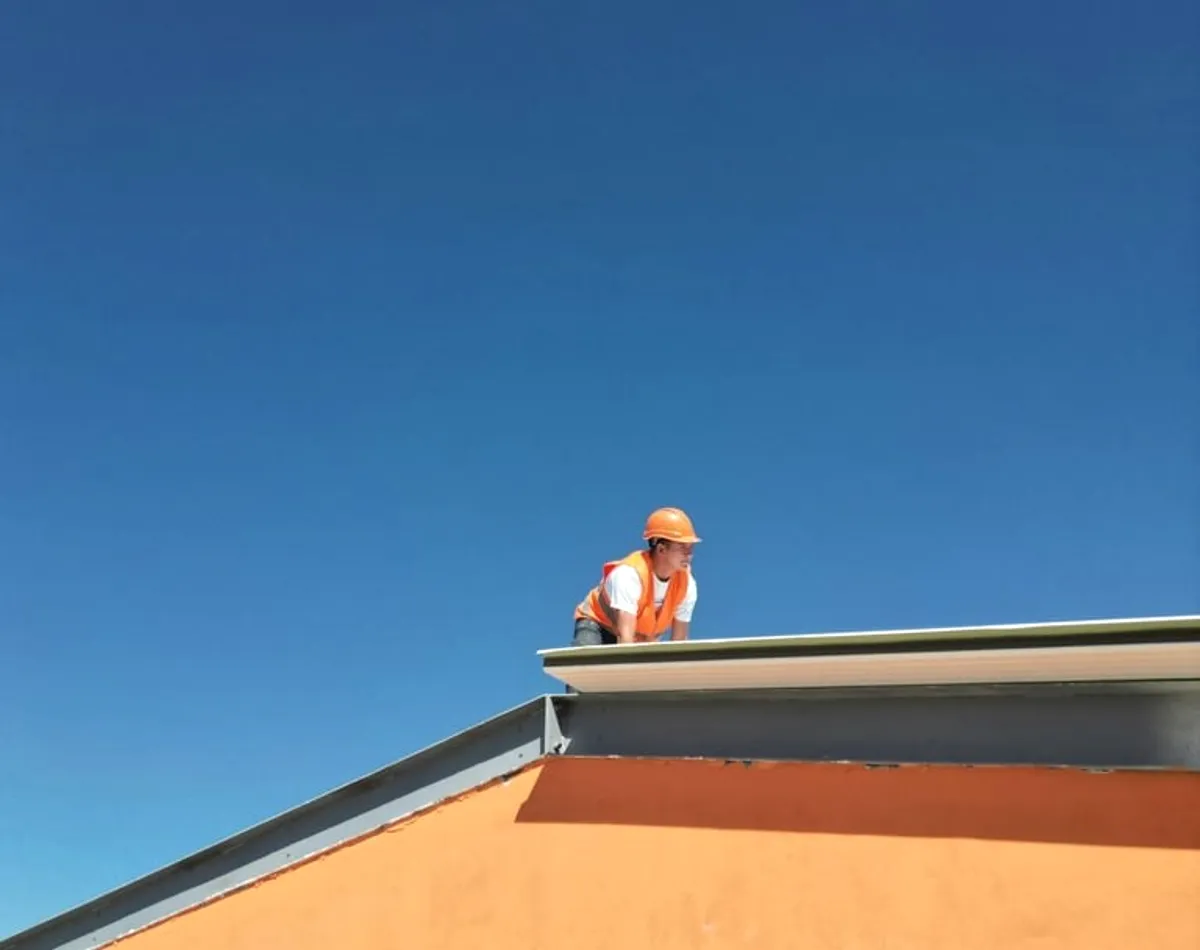 A roofer in orange on a roof against blue sky.
