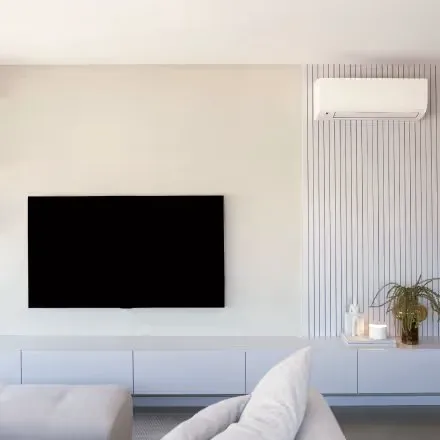 A living room with an air conditioner above a wall-mounted screen.