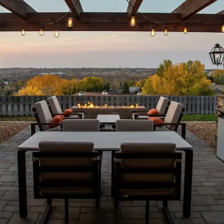 An outdoor terrace with cushioned chairs around a fire pit at dusk.