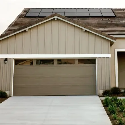 A house front with a closed garage door and solar panels on the roof.