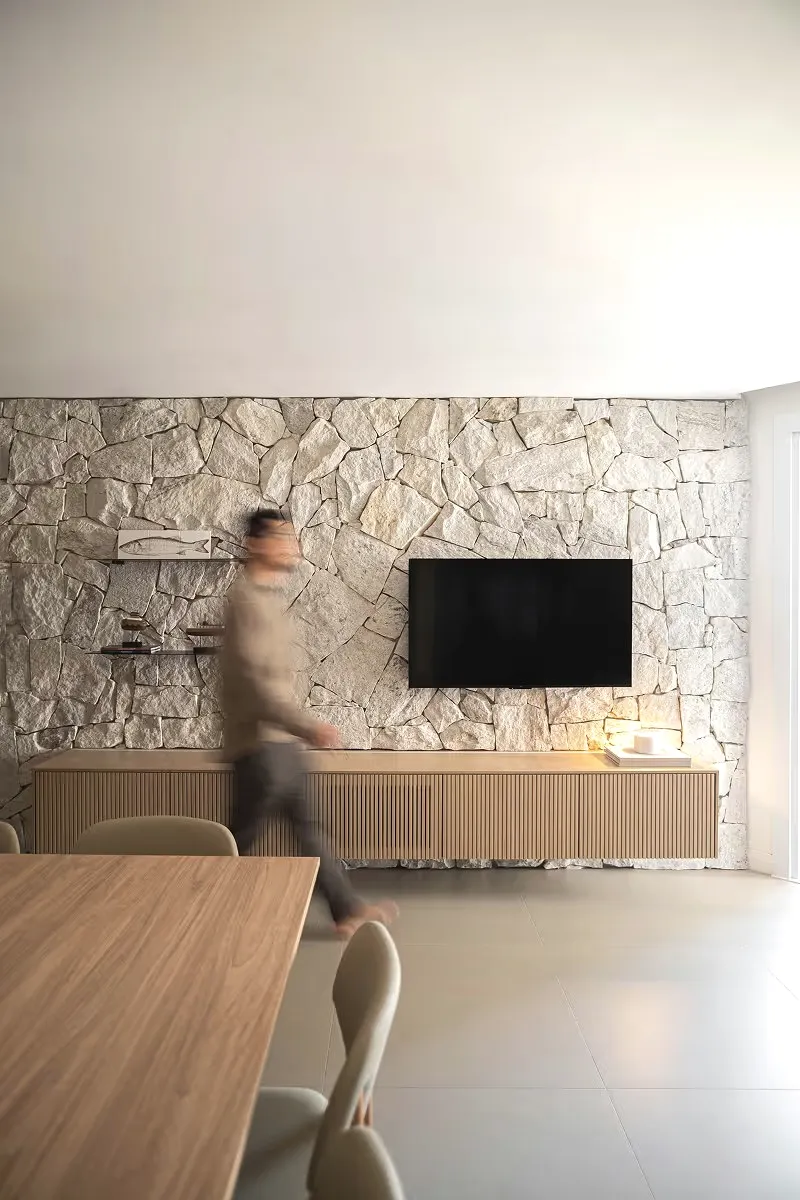 A living room with a stone wall, a wall-mounted screen and a wooden cabinet.