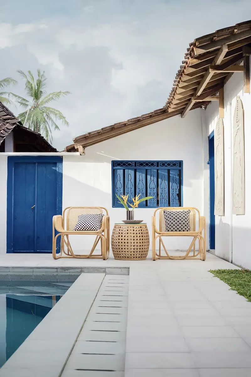 Two rattan chairs on a white patio beside a pool, blue doors behind.