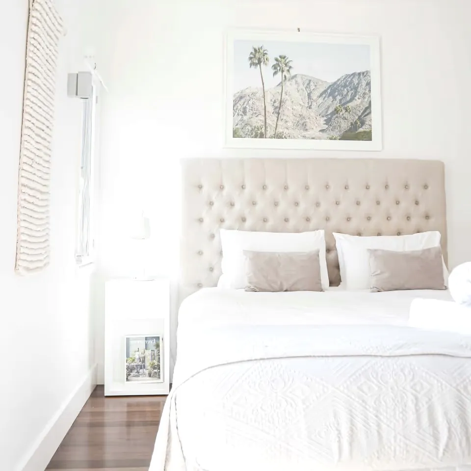 A bedroom with a tufted headboard, white bedding and a framed print.