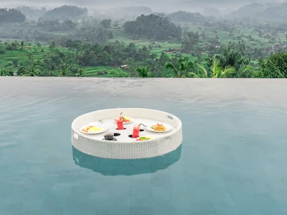 A floating breakfast tray in an infinity pool above green hills.
