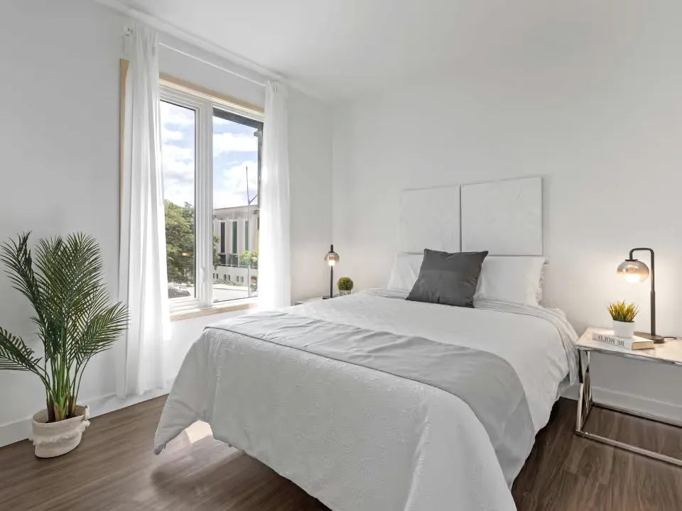 A bright bedroom with grey and white linen and a bedside lamp.