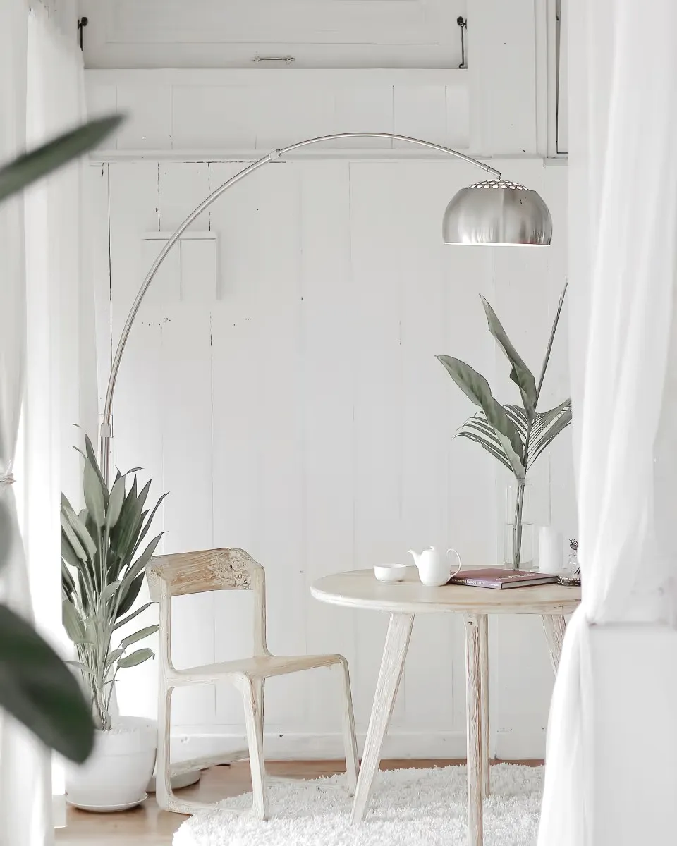 A round wooden table and one chair under an arched floor lamp.