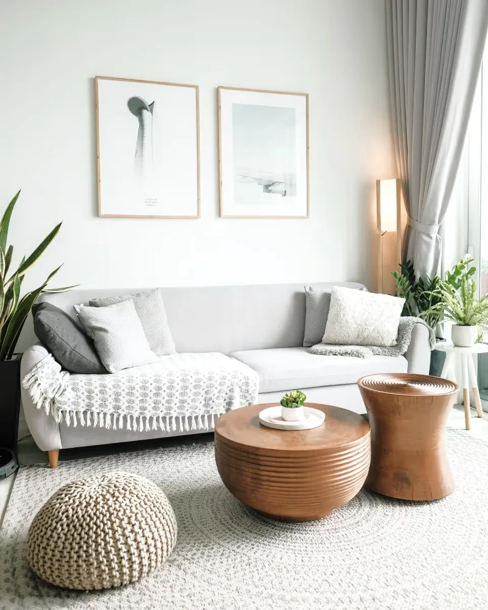 A living room with a light sofa, wooden tables and a knitted pouf.