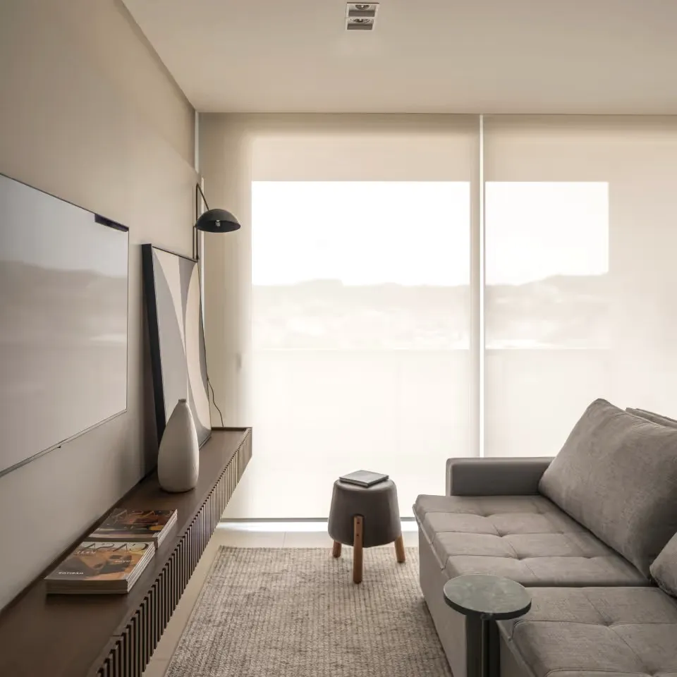 A living room with a grey sofa, a stool and a screen on the wall.