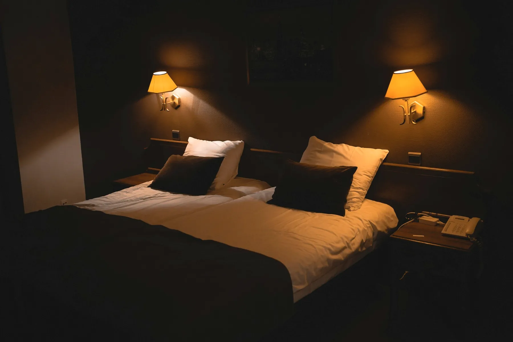 A made bed under two wall lamps in a dim room.