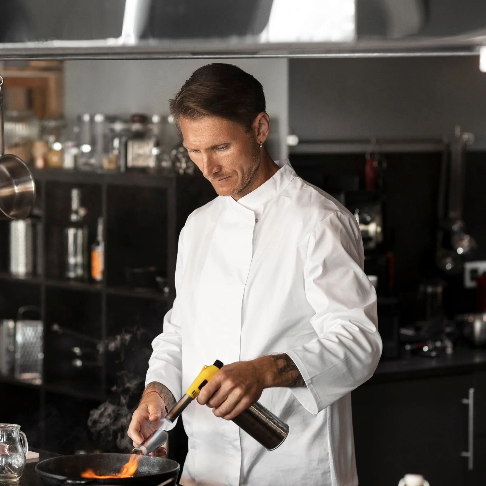 A chef in whites finishing a dish with a torch.