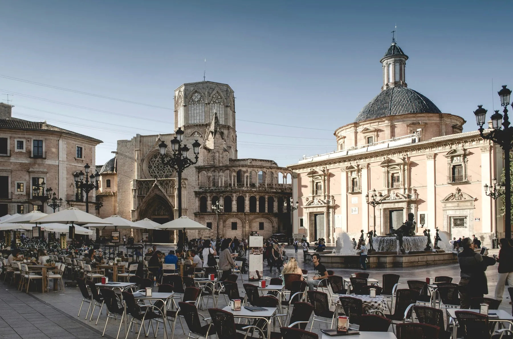 A city square with a cathedral and cafe tables.