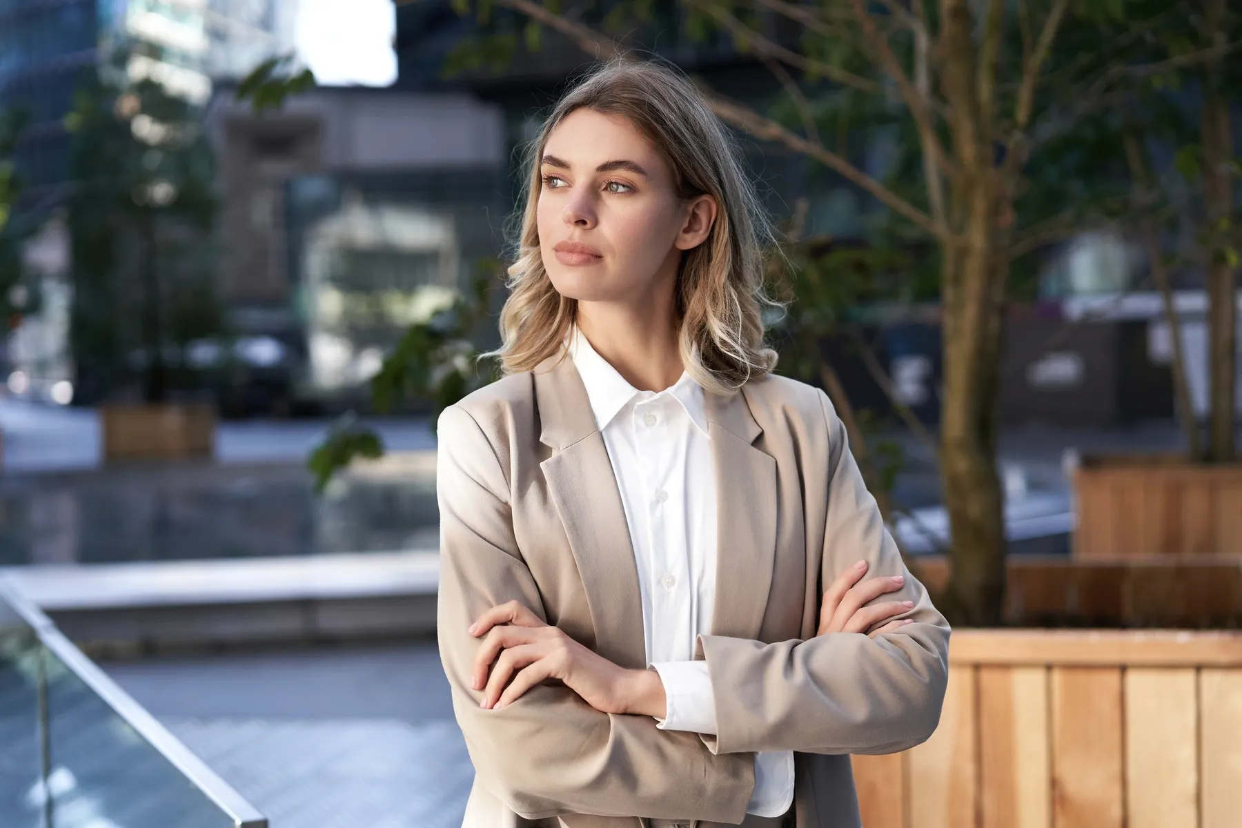 A woman in a blazer outdoors, arms crossed.