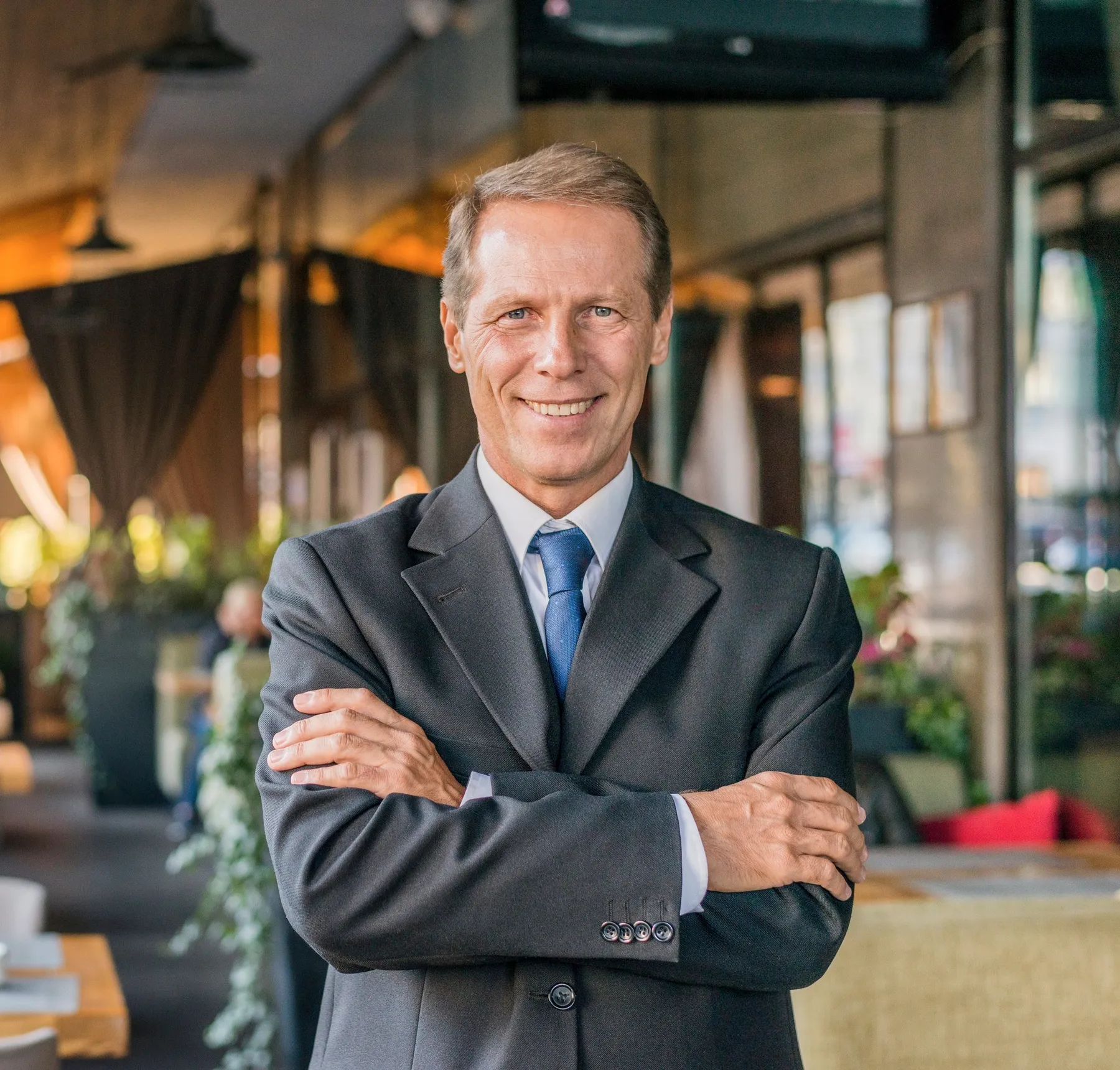 A man in a suit with arms crossed in a lobby.