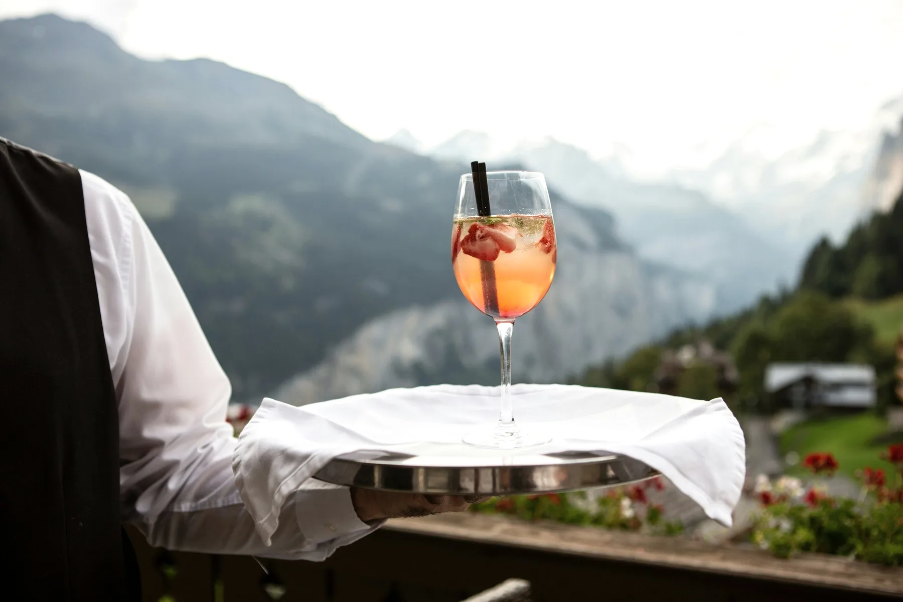 A waiter's tray with a spritz, mountains behind.