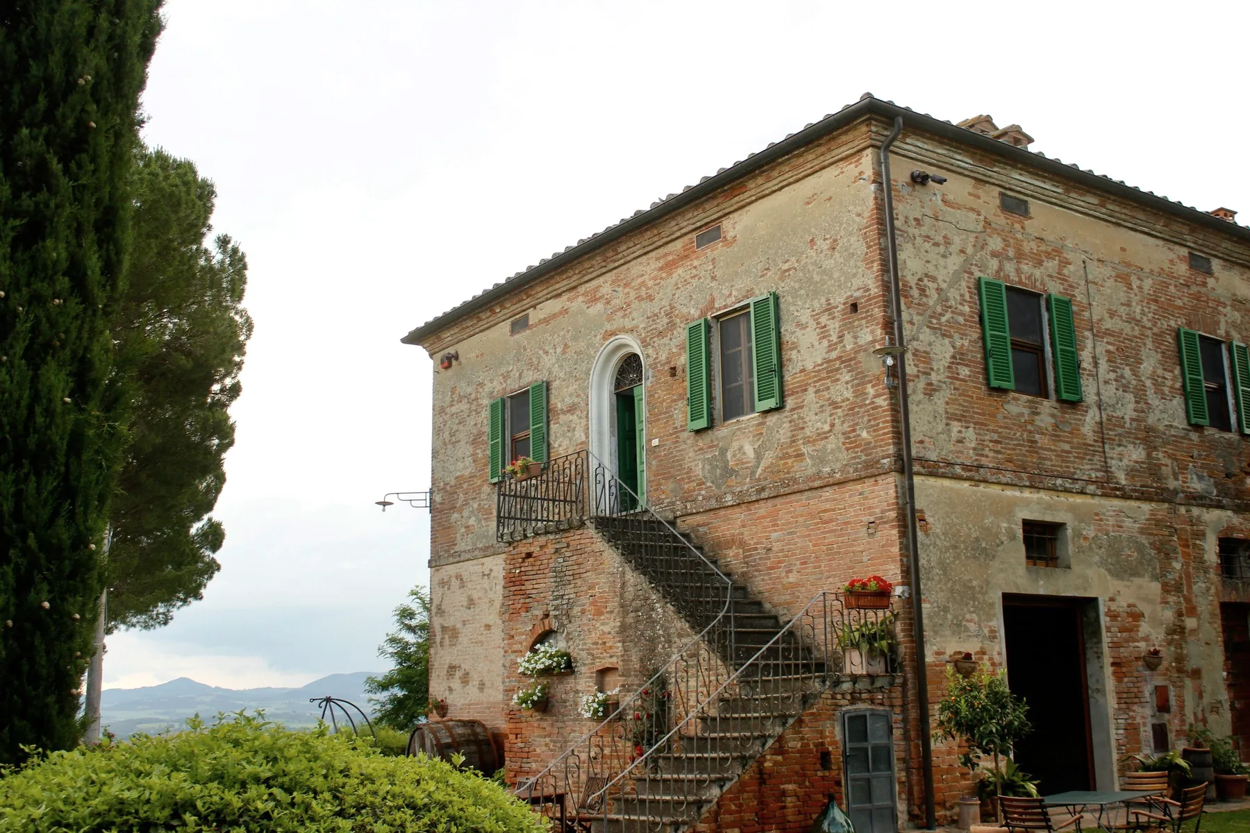 A brick farmhouse with green shutters and an outside stair.