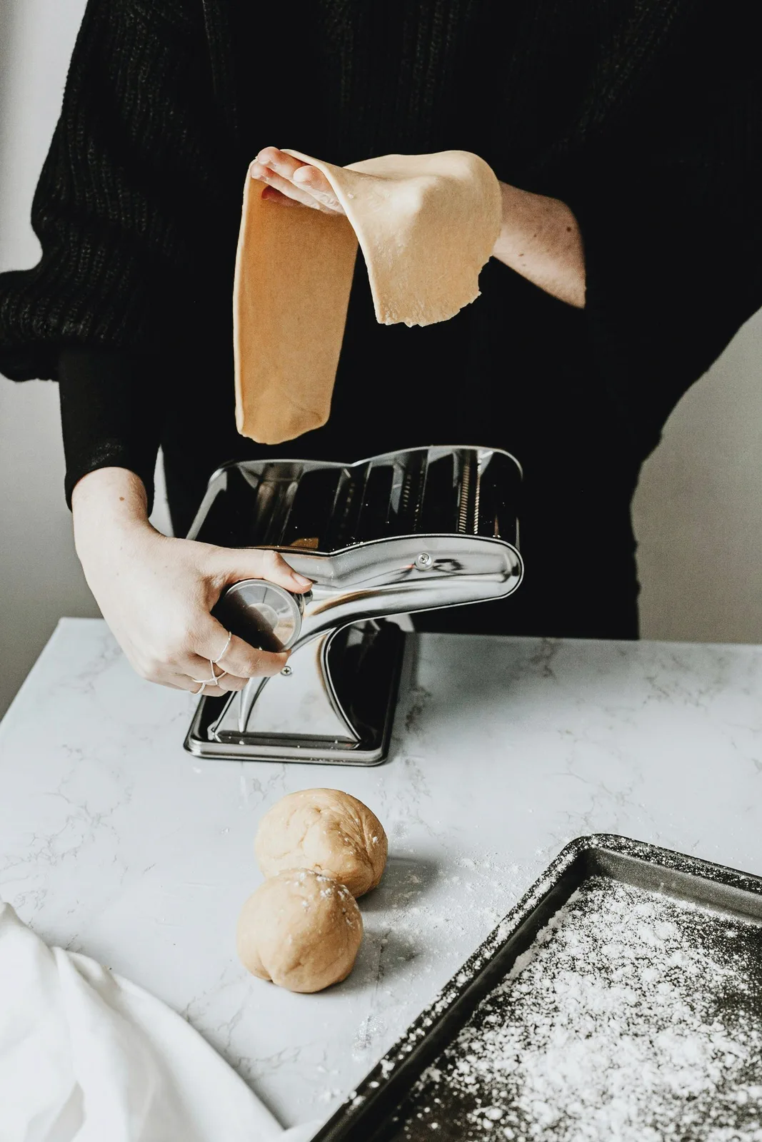 Hands turning a pasta machine on a marble counter.