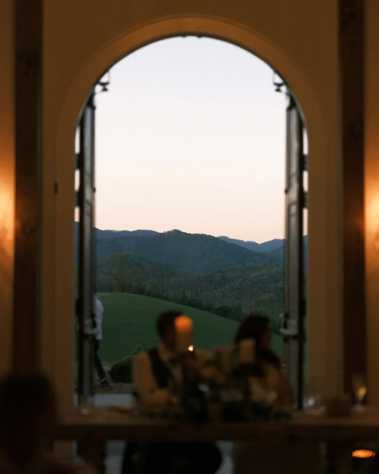 An arched window at dusk over a candlelit dinner.