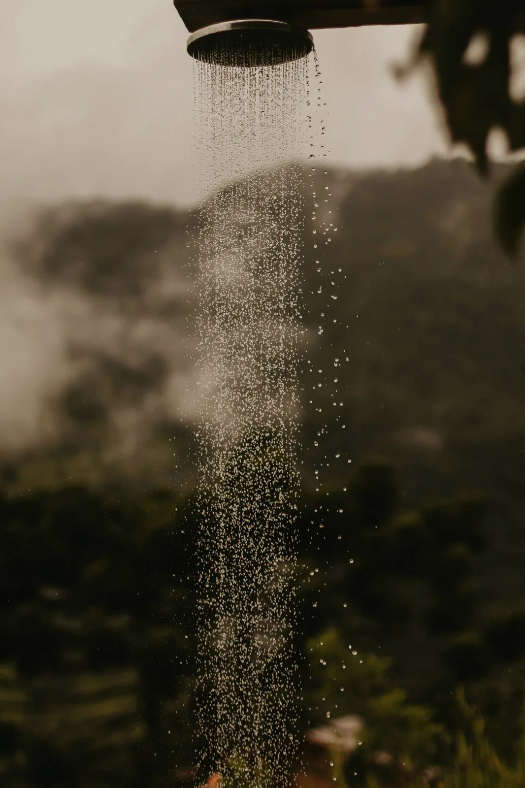 An outdoor shower head, water falling against the hills.