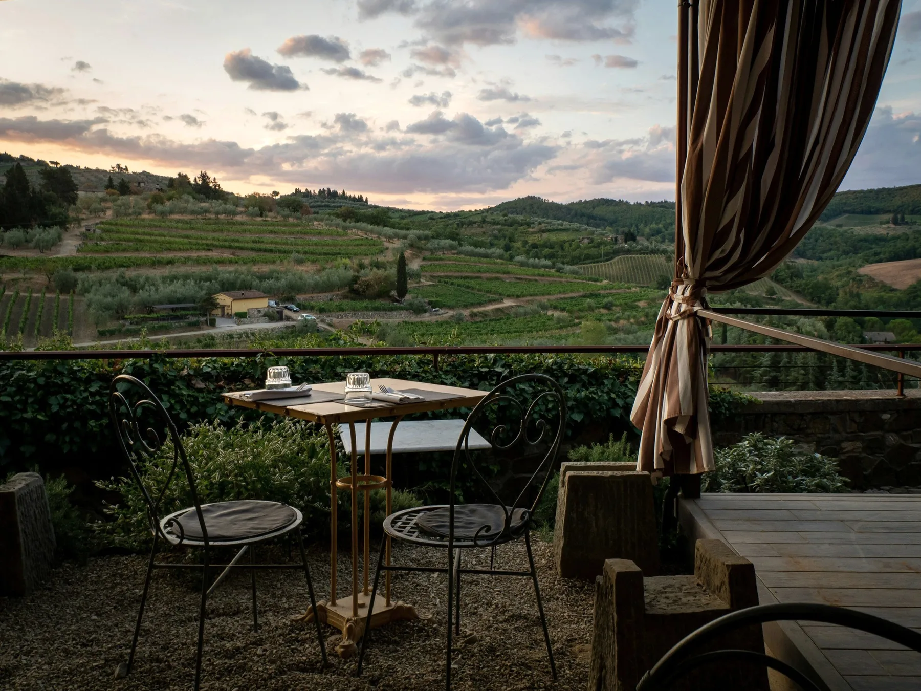 A terrace table under a striped curtain, vineyards below.