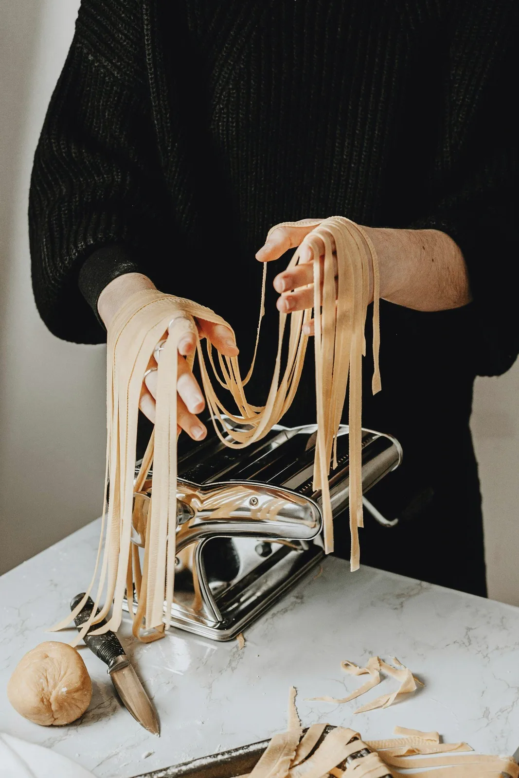 Hands lifting fresh tagliatelle from a pasta machine.