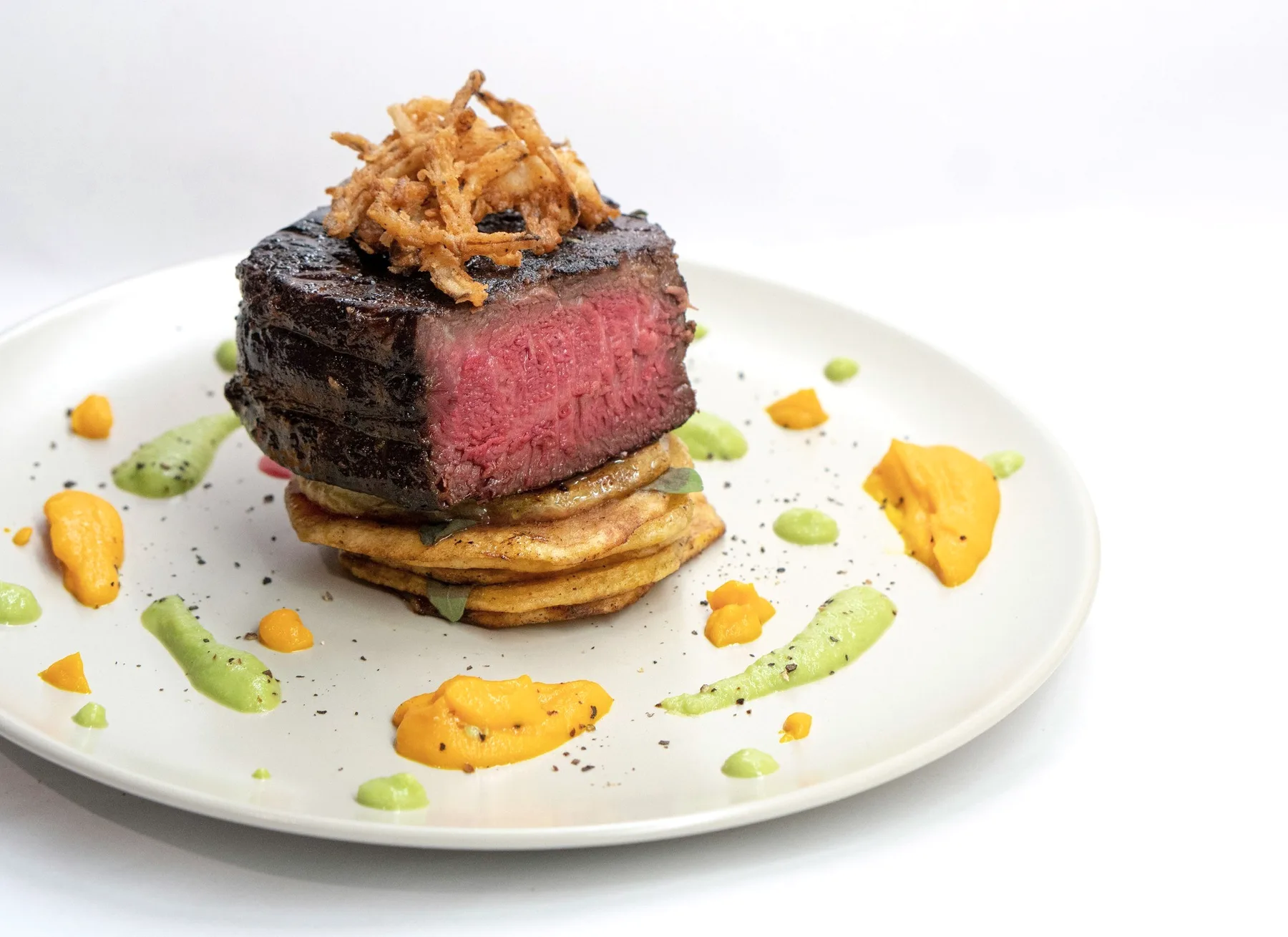 A seared fillet on a white plate with dots of sauce.