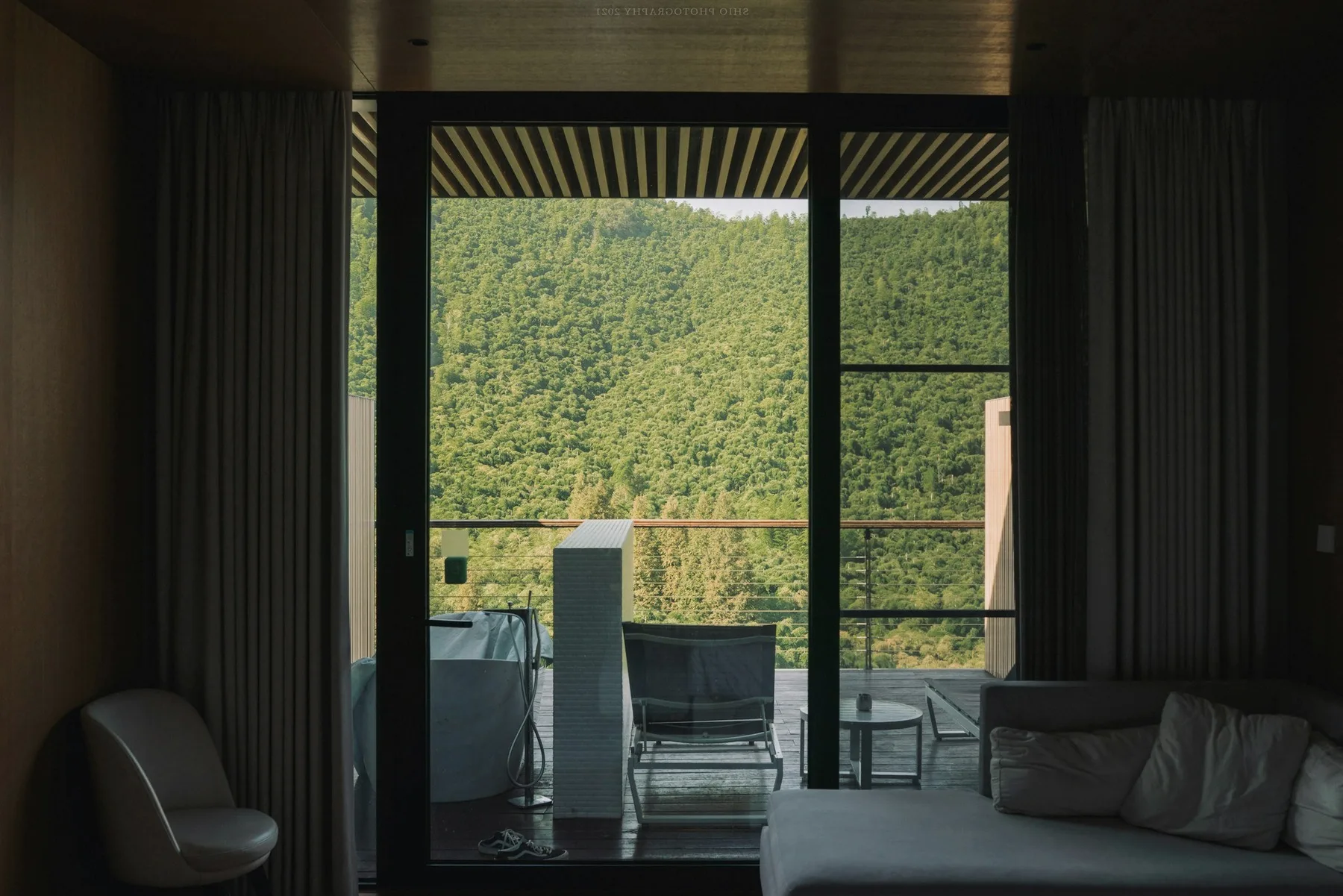 A room open to a terrace, wooded hills beyond the glass.