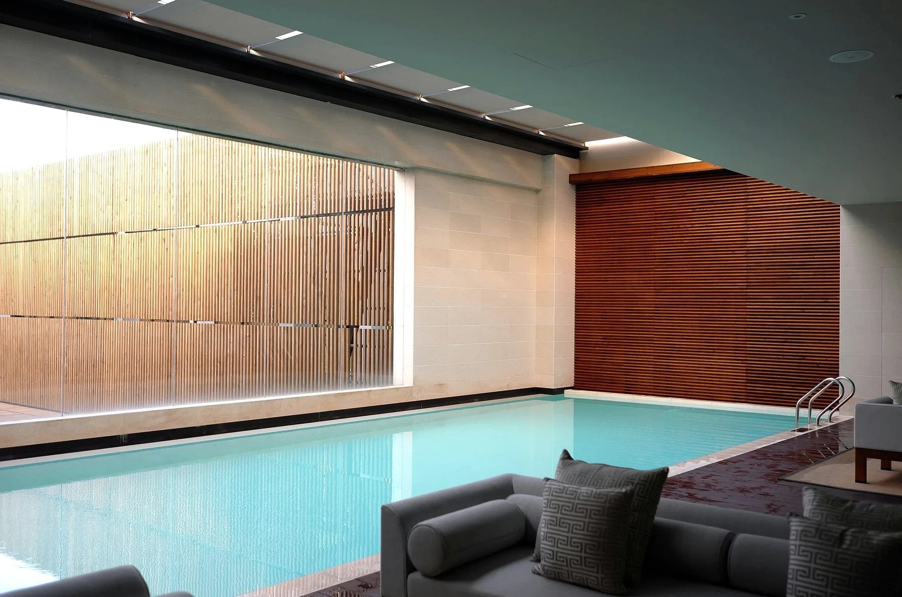 An indoor pool with wooden slats and a grey sofa.