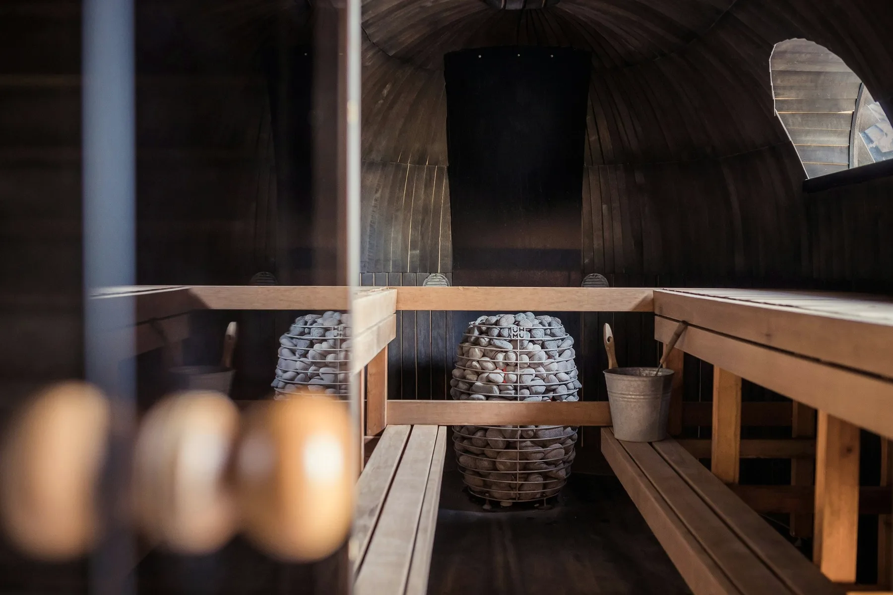A wooden sauna with a bucket and a basket of stones.