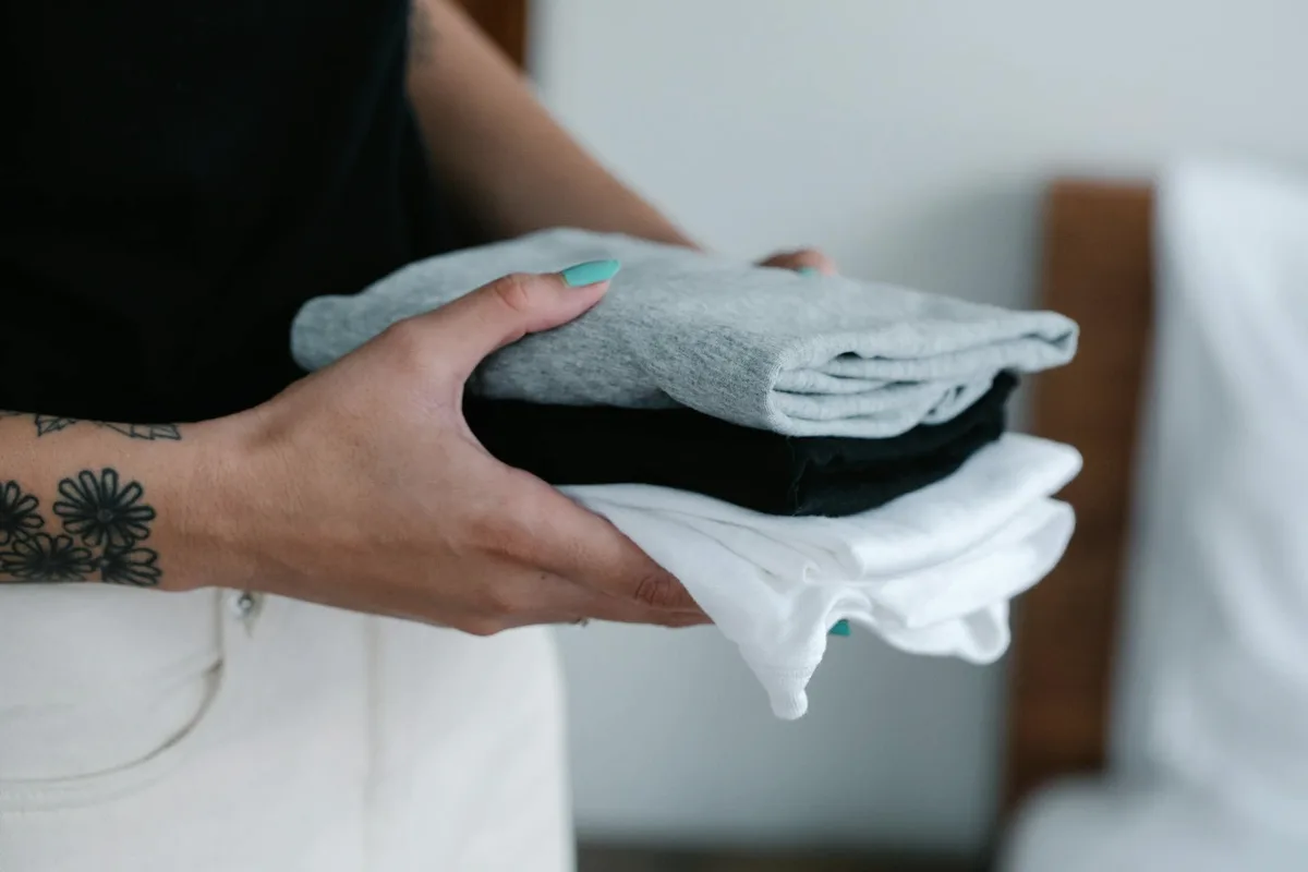 Hands holding a stack of folded clothes.