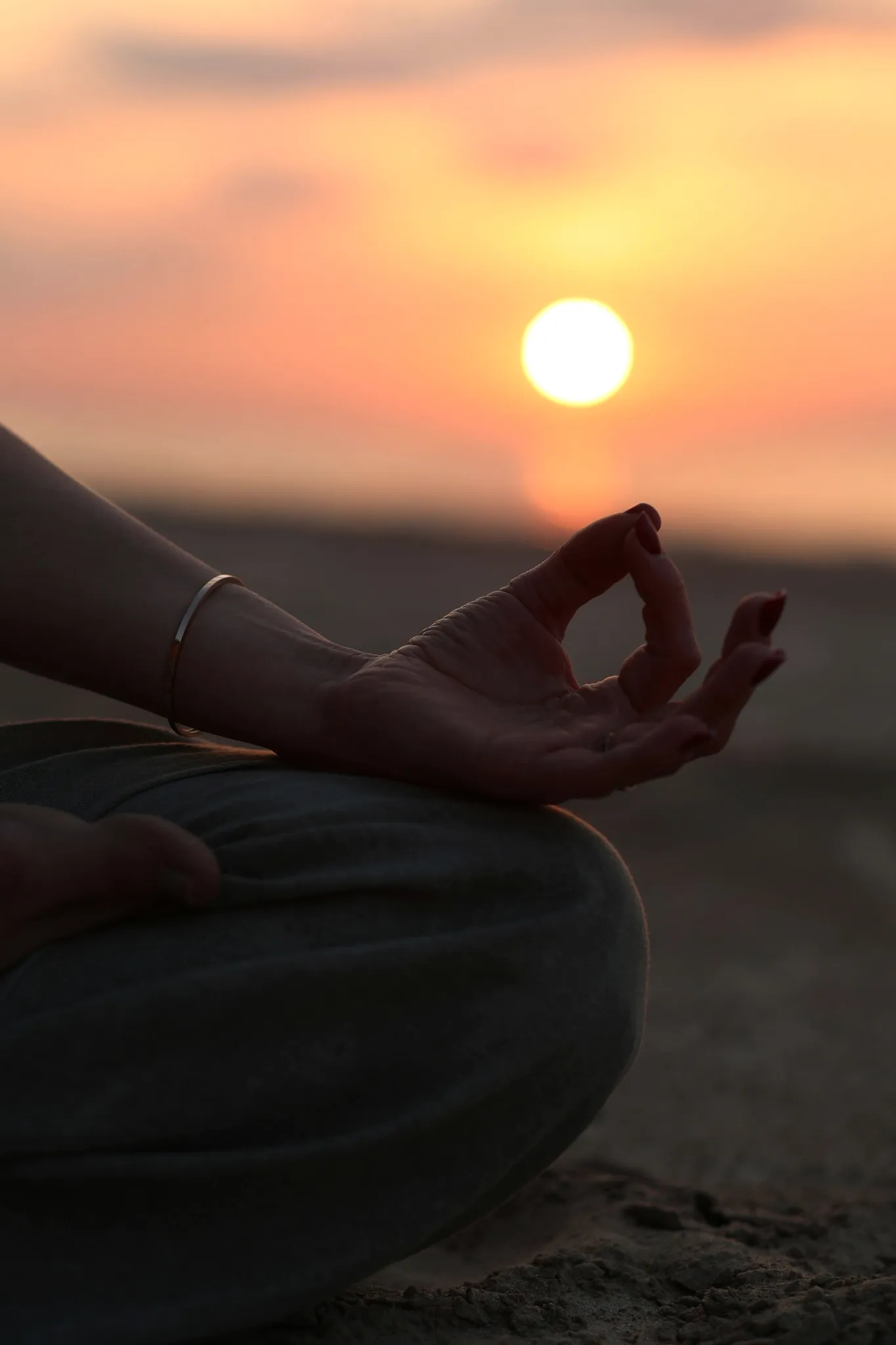 A hand resting in a meditation mudra against a sunrise.