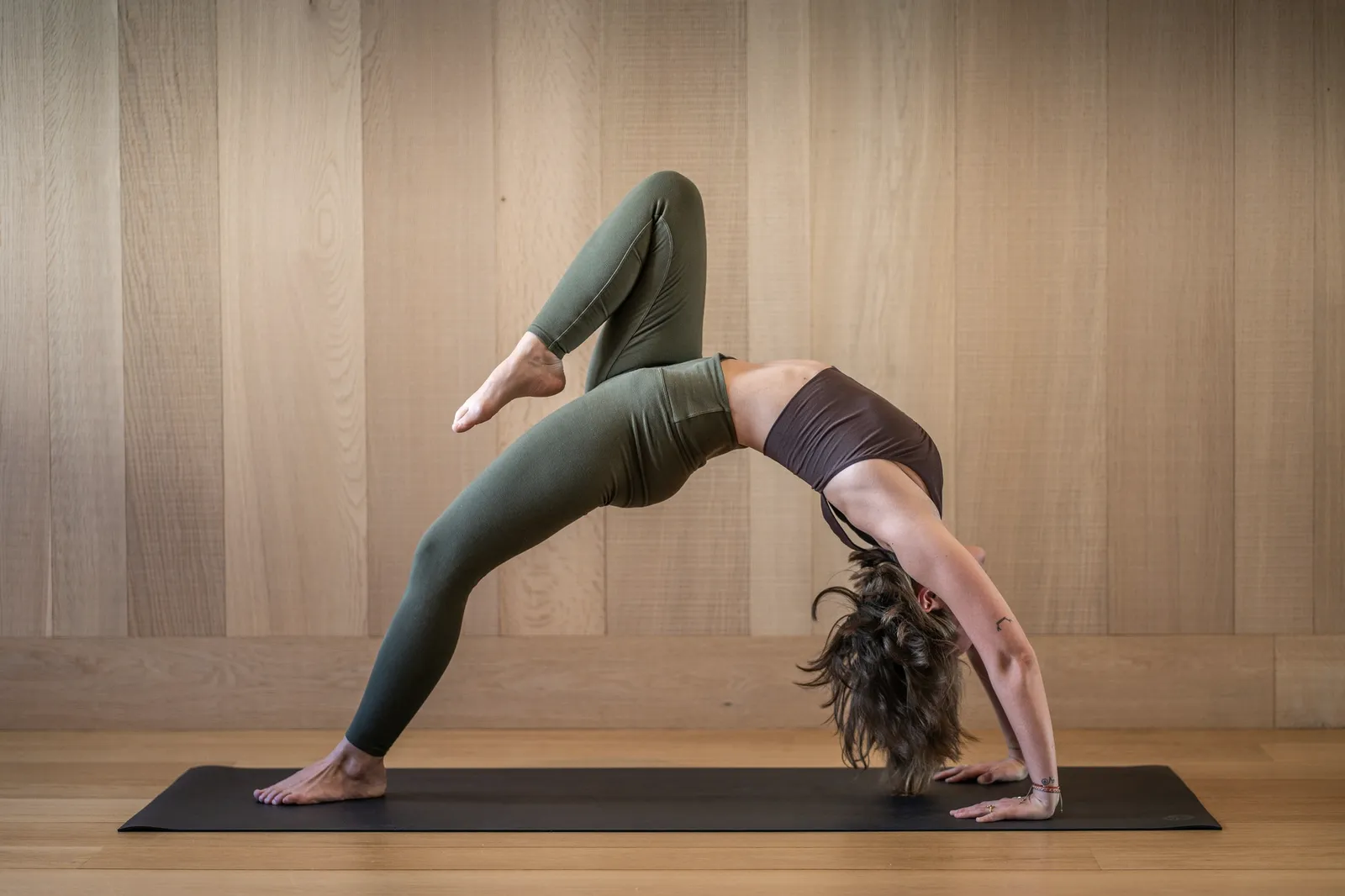 A deep backbend held on a mat in a wood-panelled room.