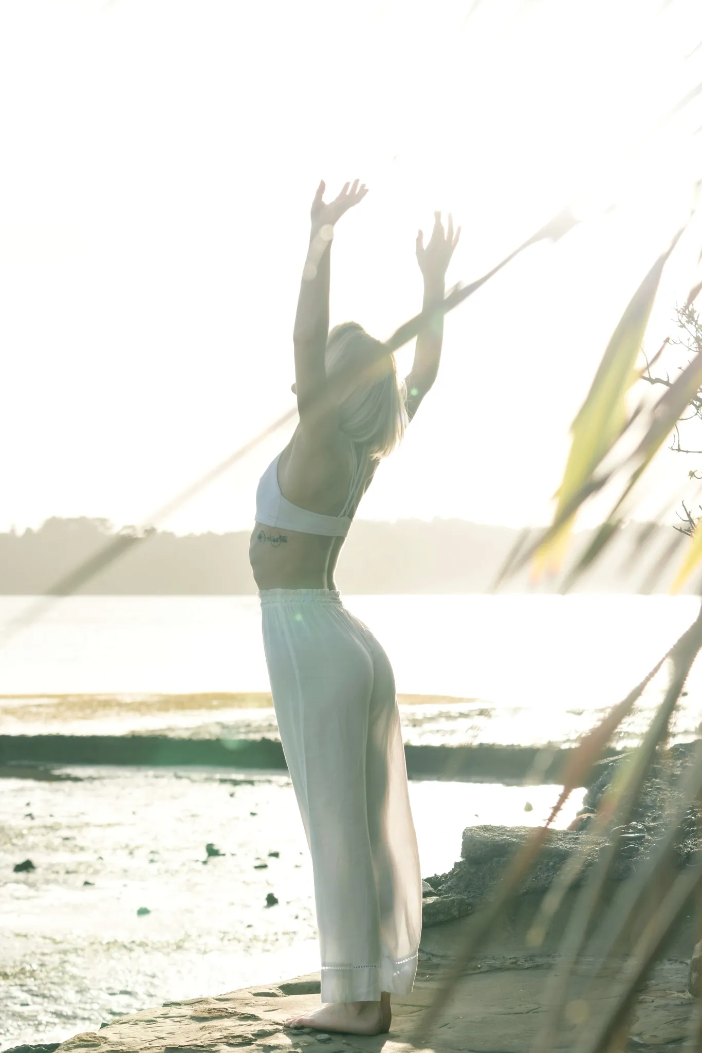 A person stretching upward in bright sunlight by the sea.