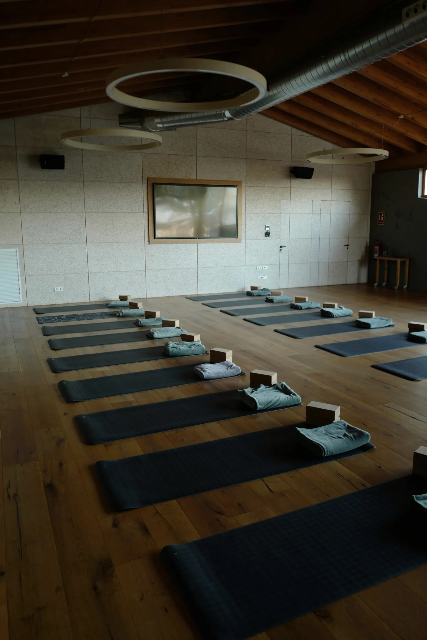 A studio with rows of mats, blocks and folded towels on a wooden floor.