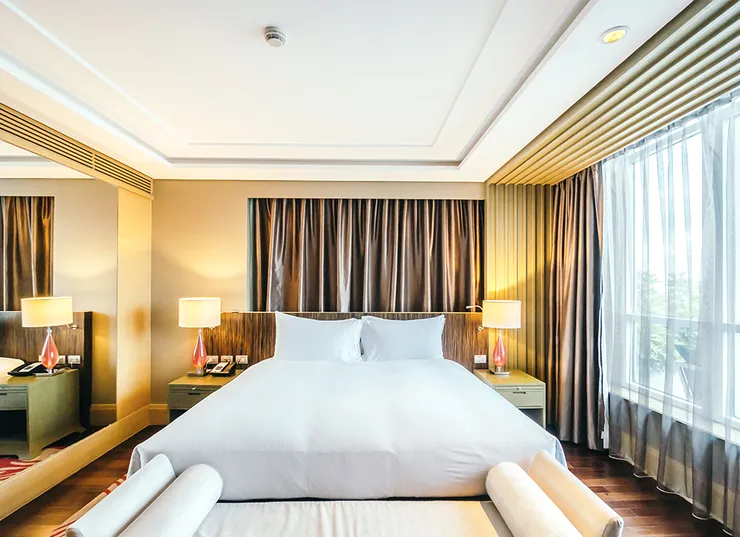 A hotel bedroom with a wide bed and brown curtains.