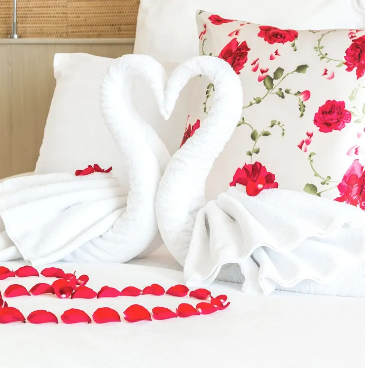 Two towel swans on a bed with red petals.
