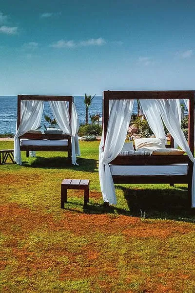 Two canopy beds on a lawn by the sea.