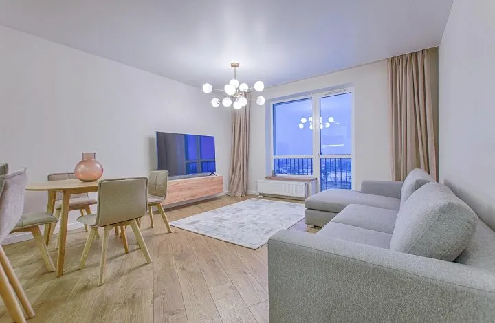 A bright living area with a grey sofa, a round dining table and a chandelier.