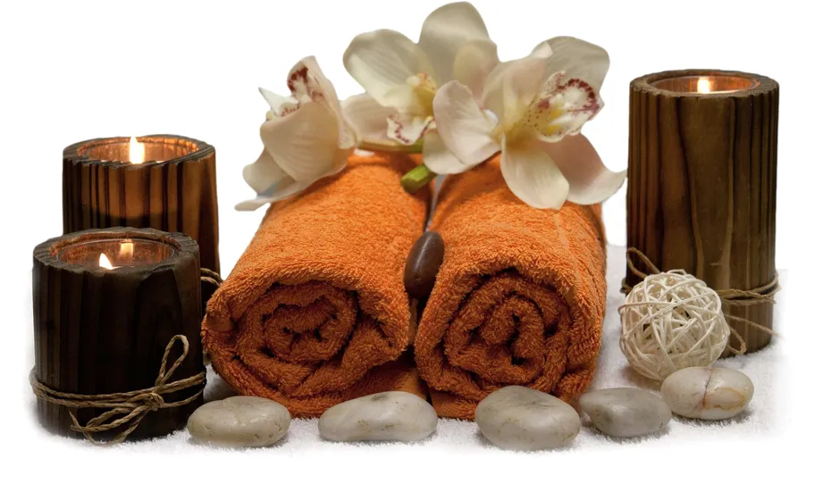 Rolled orange towels, candles, stones and white orchids.